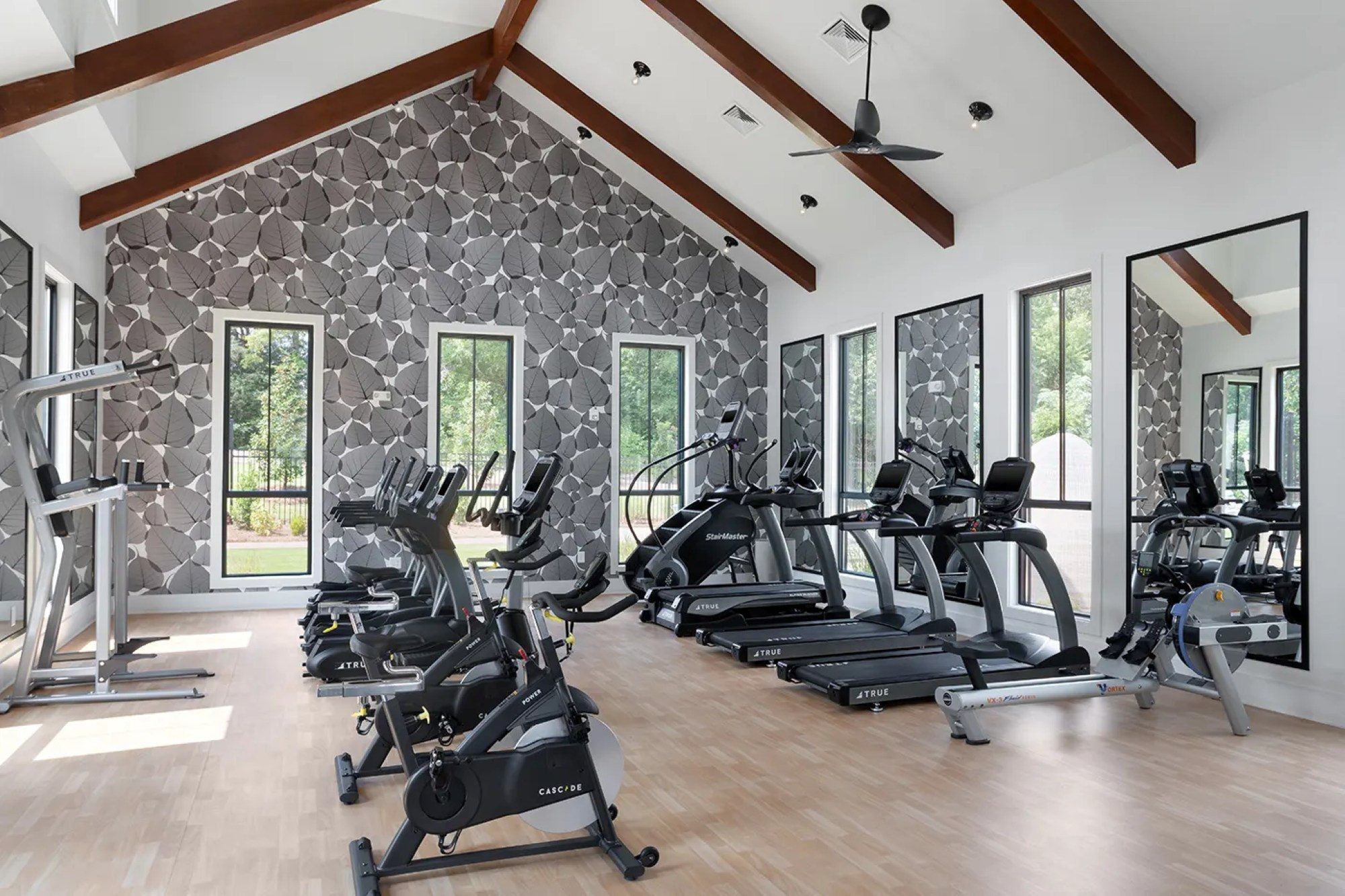 Fitness center with vaulted wood-beamed ceilings, leaf-patterned wallpaper, exercise bikes, and treadmills.